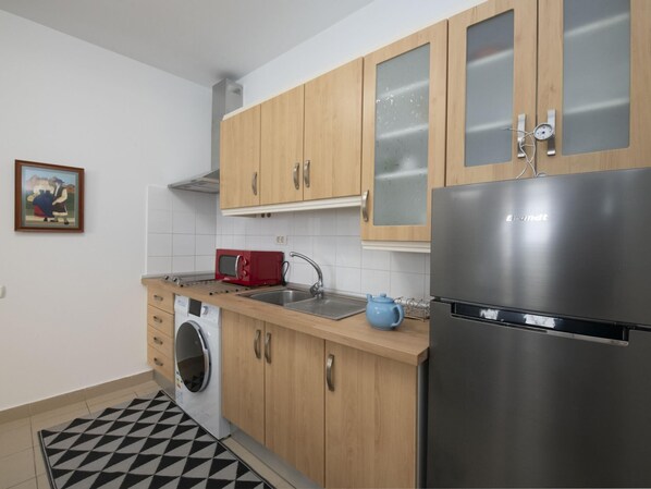 Eine moderne Küche mit Holzausstattung, einem Edelstahlkühlschrank, einer Waschmaschine und einer roten Mikrowelle.