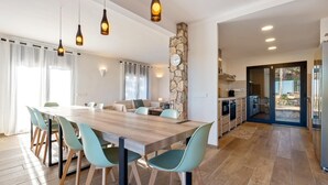 Une cuisine moderne avec un mur d’accent en pierre, un coin repas avec une table en bois et des chaises turquoise, et une vue sur l’espace extérieur grâce à une porte vitrée.