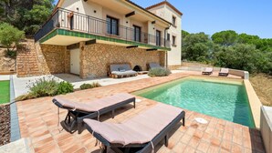 Une maison à deux étages avec une façade en pierre, un balcon, une piscine et un espace salon extérieur.