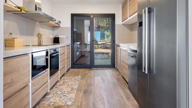 Une cuisine moderne avec des meubles en bois, des appareils électroménagers en acier inoxydable et un tapis à motifs.