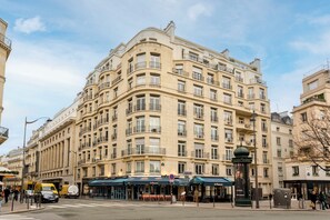 A multi-story hotel with a classic architectural style, featuring balconies and a ground-level restaurant with outdoor seating.