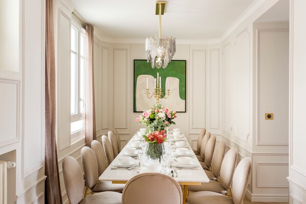 Un comedor formal con una larga mesa dispuesta para ocho personas, una araña y un cuadro abstracto enmarcado en la pared.