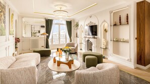 A spacious living room with a chandelier, a fireplace, and a television. - Merveil Signature Suite Hoche - Eiffel Tower view (Paris)
