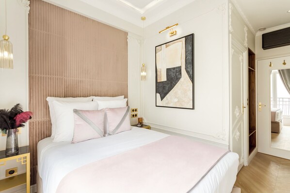 A bedroom with a large bed, a bedside table with a lamp, a wall-mounted artwork, and a wardrobe.