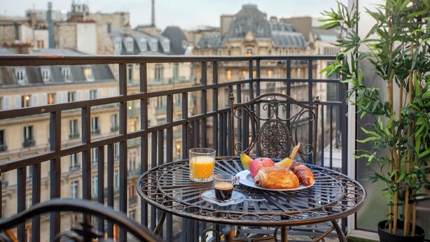A balcony with a metal table, a chair, and a potted plant. - Merveil Signature Suite Hoche - Eiffel Tower view (Paris)