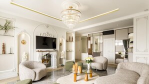 A modern living room with a chandelier, sofas, a fireplace, and a television. - Merveil Signature Suite Hoche - Eiffel Tower view (Paris)