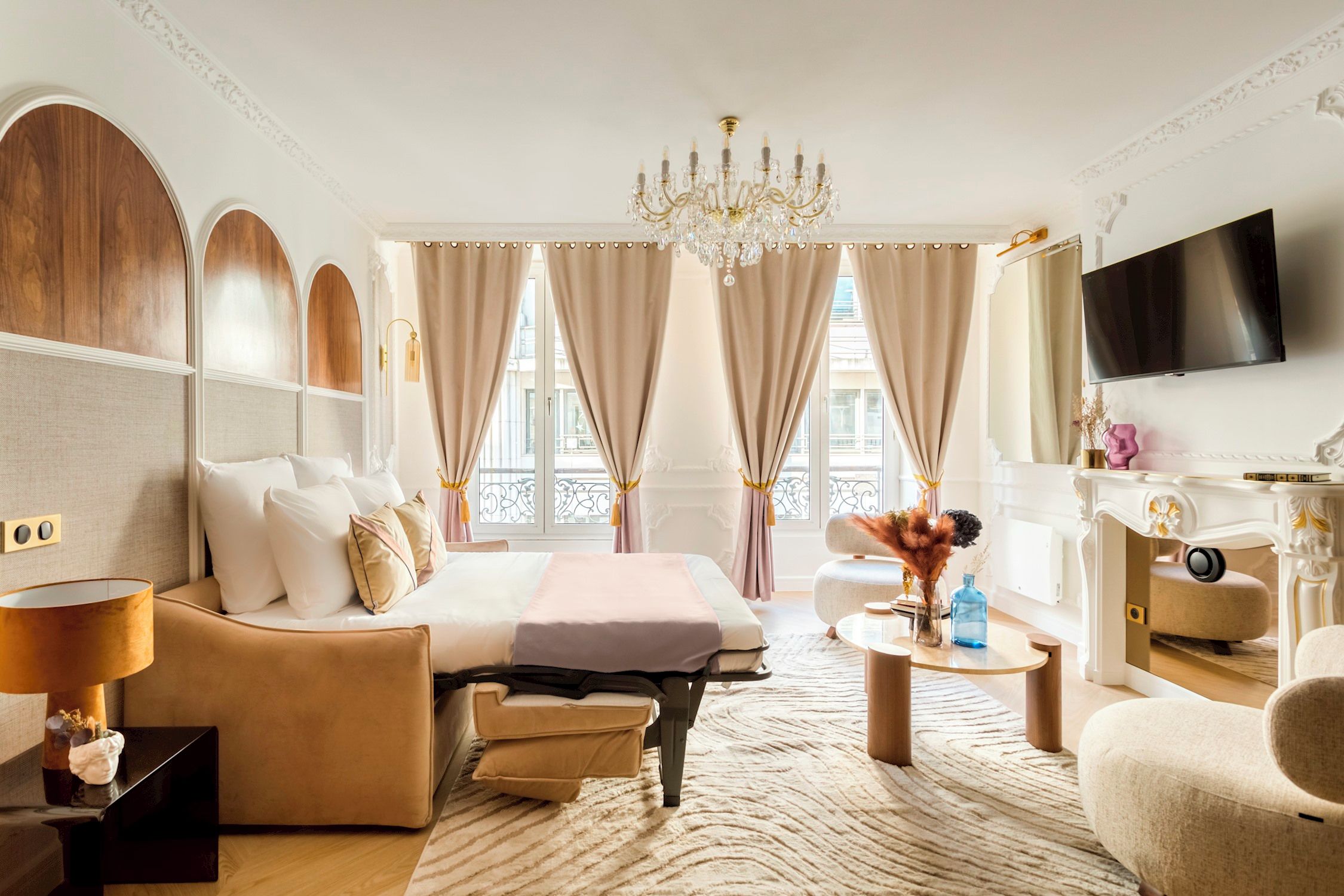 Une chambre d’hôtel avec un lit, un canapé, une télévision, un lustre et une vue sur l’extérieur.