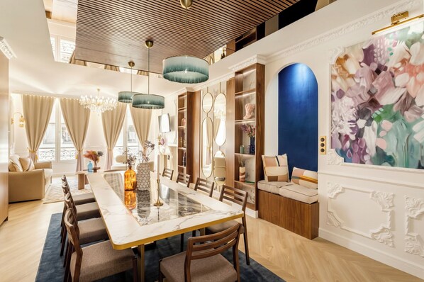 Uma sala de jantar ampla com uma mesa de mármore, cadeiras de madeira e um candelabro.