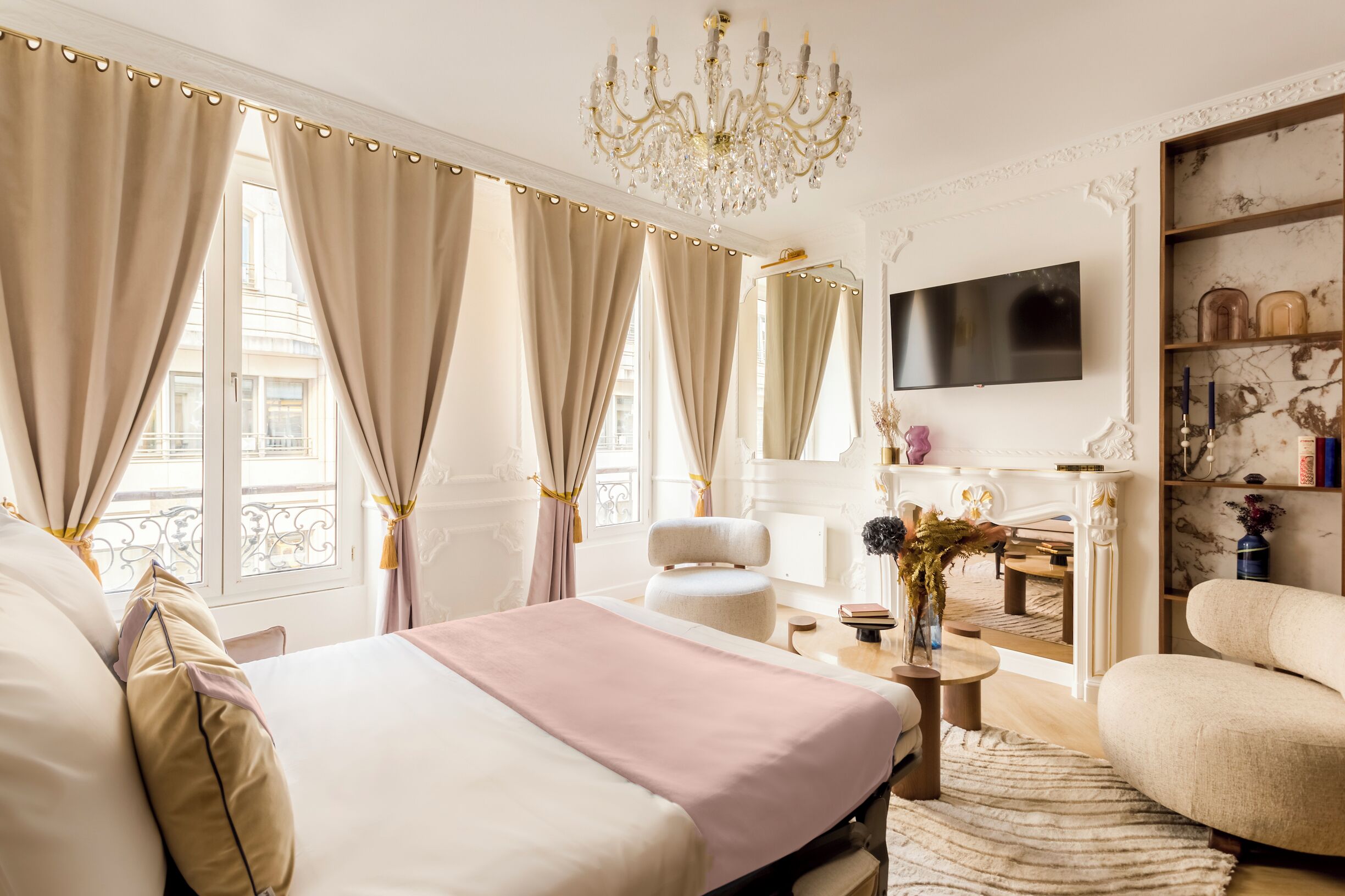 A spacious bedroom with a large bed, a sitting area with a chair, a television, and a bookshelf.