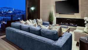 A modern living room with a large blue sofa, a flat-screen TV mounted on the wall, and a fireplace. - New Ski-In/Out Ultra Luxe Deer Valley Condo in Intimate Lodge. Superb restaurant (Park City)