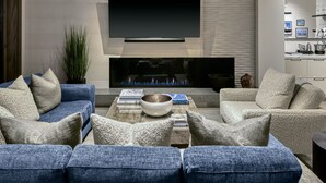 A modern living room with a flat-screen TV mounted above a fireplace, a coffee table with books and a bowl, and a seating area with sofas and cushions. - New Ski-In/Out Ultra Luxe Deer Valley Condo in Intimate Lodge. Superb restaurant (Park City)