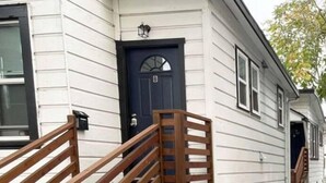 Un edificio blanco con una puerta azul oscuro, una escalera de madera y un pequeño porche.