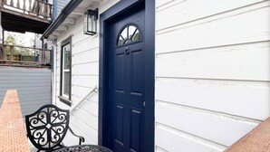 Un edificio blanco con una puerta azul oscuro, un pequeño porche con una silla y un banco de madera.