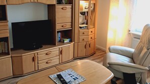 A living room with a TV, wooden furniture, a sofa, and a window with curtains.