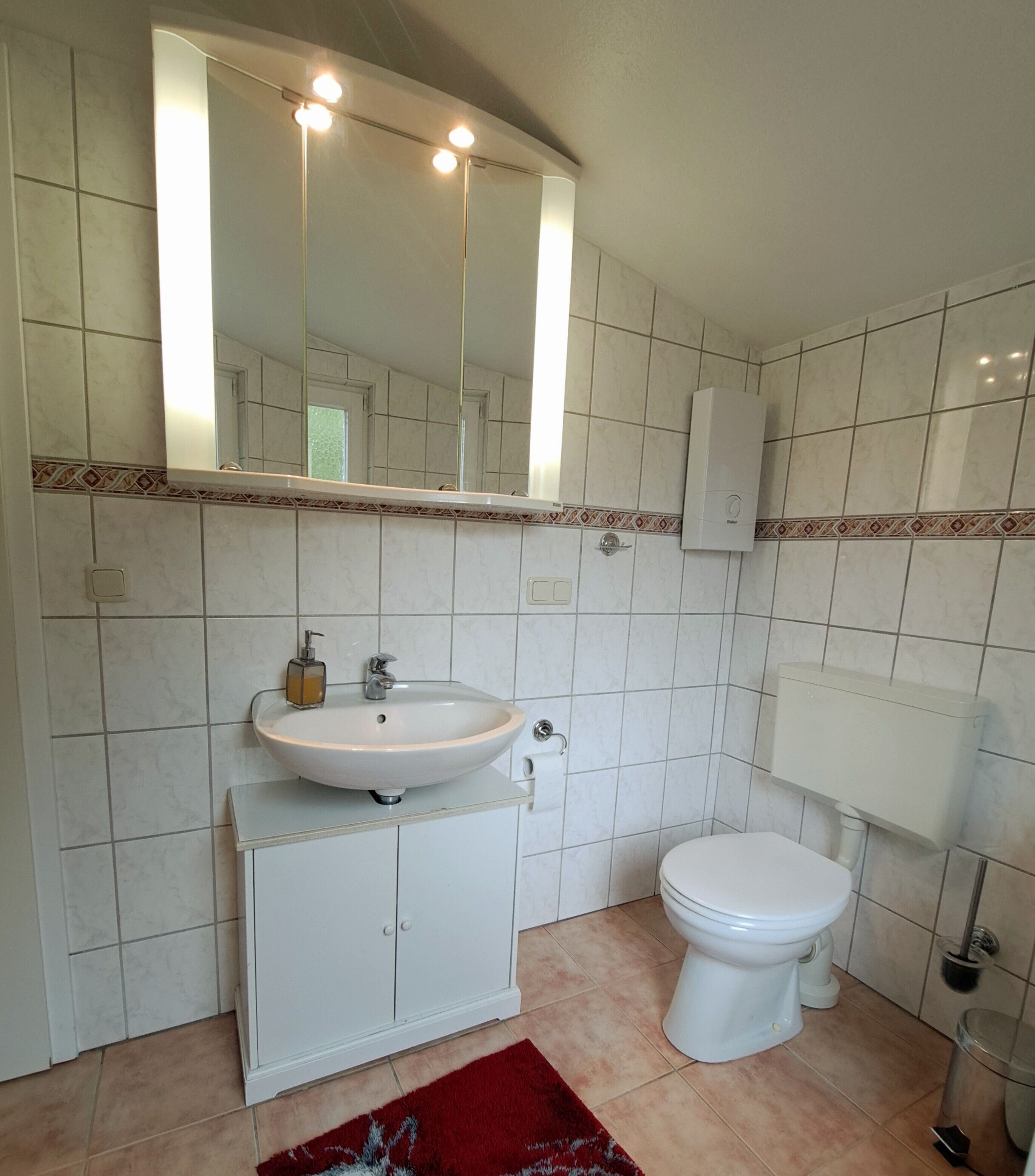 A bathroom with a white sink, a toilet, a mirror, and a hand dryer.