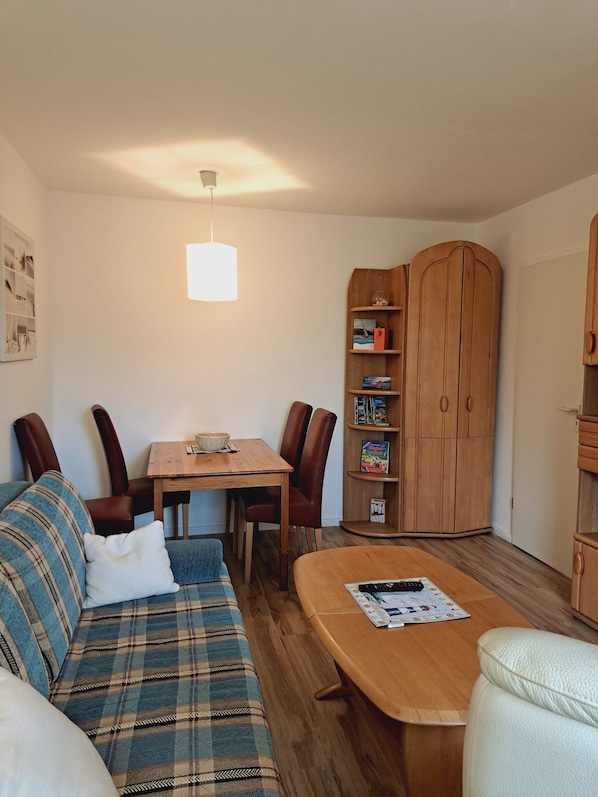 A cozy living area with a sofa, a wooden coffee table, a dining table with chairs, and a wooden cabinet with shelves.