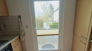 A kitchen with a sliding door leading to a garden, tiled floor, and a black mat.