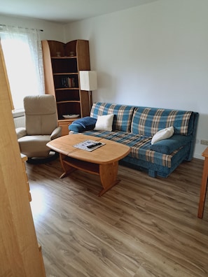A living room with a sofa, armchair, wooden coffee table, bookshelf, and a lamp.