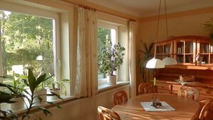 A dining room with a round table, chairs, a cabinet with shelves, and a window with curtains. - Apartment 'Heidtschmidhof Abendsonne' with Shared Terrace, Shared Garden and Wi-Fi (Wolgast)