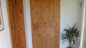 A wooden door with a metal handle, a potted plant to the right, and a tiled floor. - Apartment 'Heidtschmidhof Abendsonne' with Shared Terrace, Shared Garden and Wi-Fi (Wolgast)