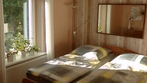A bedroom with a bed, a window with plants, a wooden wall panel, and a mirror. - Apartment 'Heidtschmidhof Abendsonne' with Shared Terrace, Shared Garden and Wi-Fi (Wolgast)