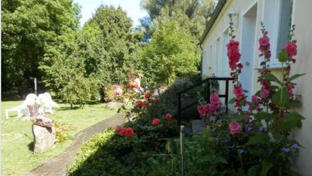 A garden with a pathway, a white building, and pink flowers. - Apartment 'Heidtschmidhof Abendsonne' with Shared Terrace, Shared Garden and Wi-Fi (Wolgast)
