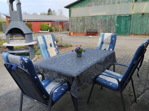 Um pátio com mesa e cadeiras, um pequeno jardim e um edifício ao fundo.