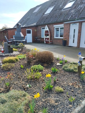 A brick building with a chimney, a garden with flowers and shrubs, and outdoor seating. - Apartment 'Wuddisferienwohnug' with Shared Terrace, Private Garden and Wi-Fi (Nordleda)