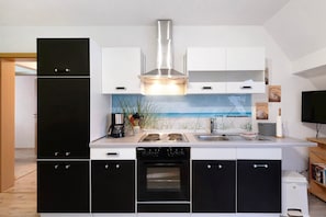 A modern kitchen with a black refrigerator, white cabinets, a stainless steel range hood, a built-in oven, and a backsplash with a beach scene. - Apartment 'Wuddisferienwohnug' with Shared Terrace, Private Garden and Wi-Fi (Nordleda)