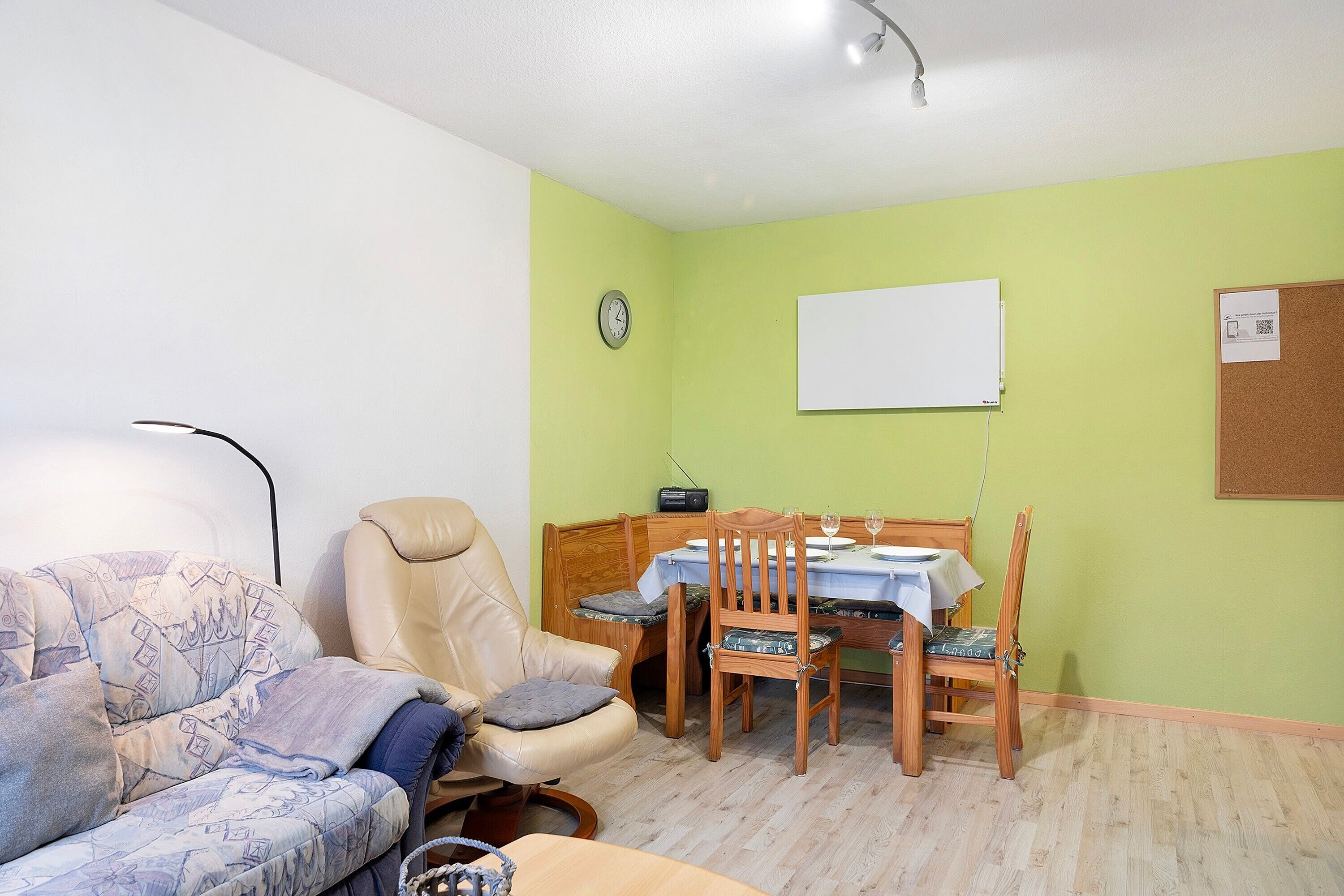 Une pièce comprenant un canapé, une table à manger avec des chaises, une horloge au mur et un tableau blanc.