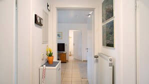 A hallway with a radiator, a clock, a television, and a door leading to another room. - Apartment 'Haus Loser' with Private Terrace, Shared Garden and Wi-Fi (Wasserburg (Bodensee))