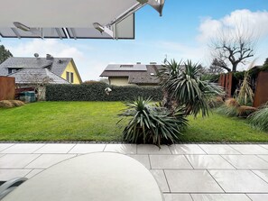 Un jardin arrière aménagé avec une terrasse, une pelouse et une haie.