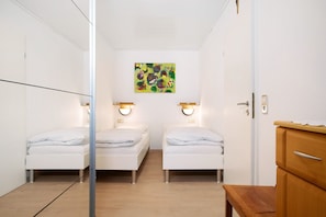 Une chambre avec deux lits, une commode en bois et un tableau accroché au mur.