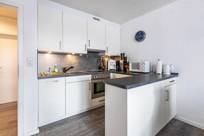 Uma cozinha moderna com armários brancos, forno embutido, micro-ondas e máquina de café.