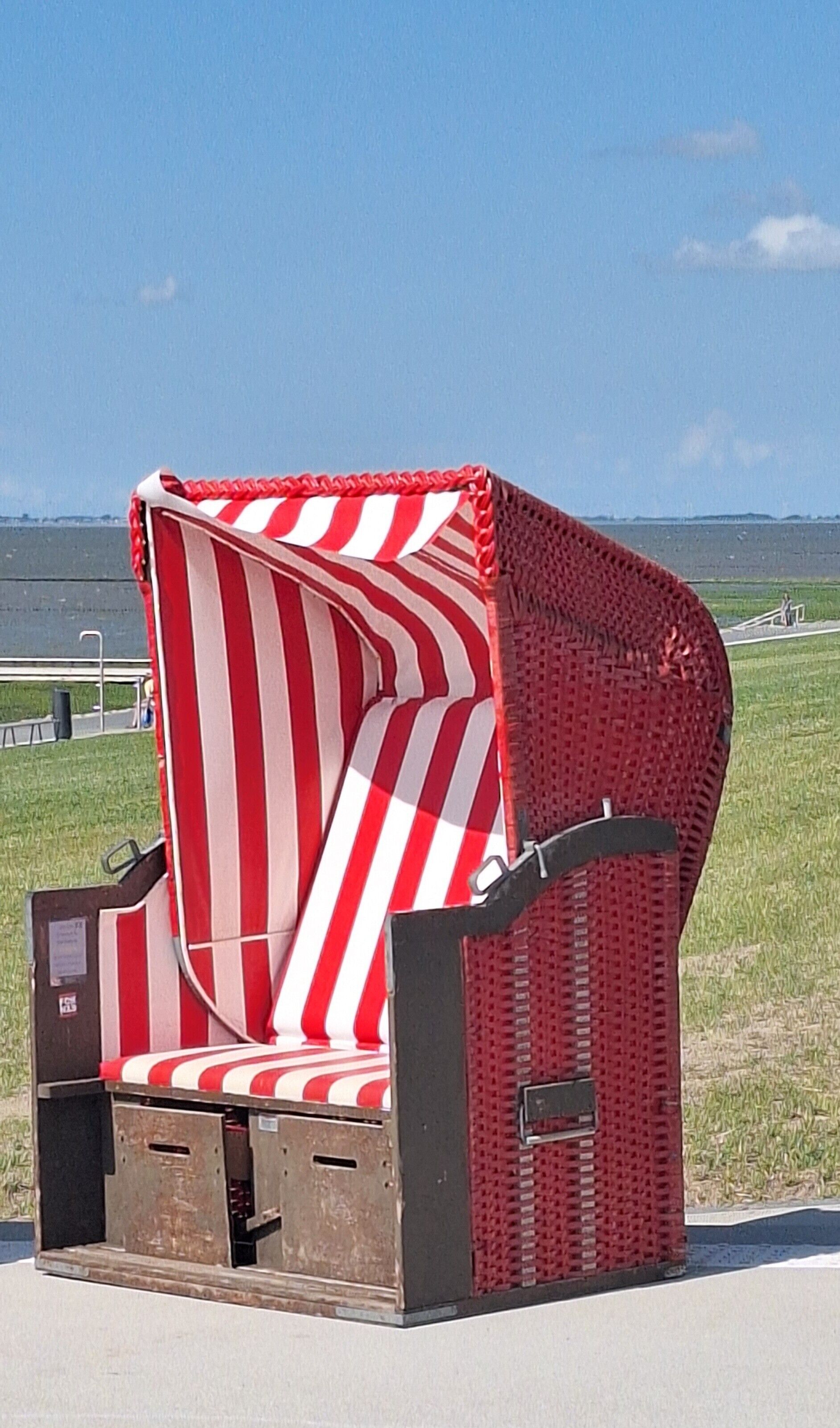 A unique, striped, curved chair with a metal frame, situated outdoors with a clear sky and distant landscape.