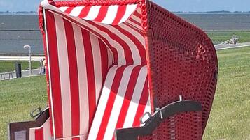 A unique, striped, curved chair with a metal frame, situated outdoors with a clear sky and distant landscape.