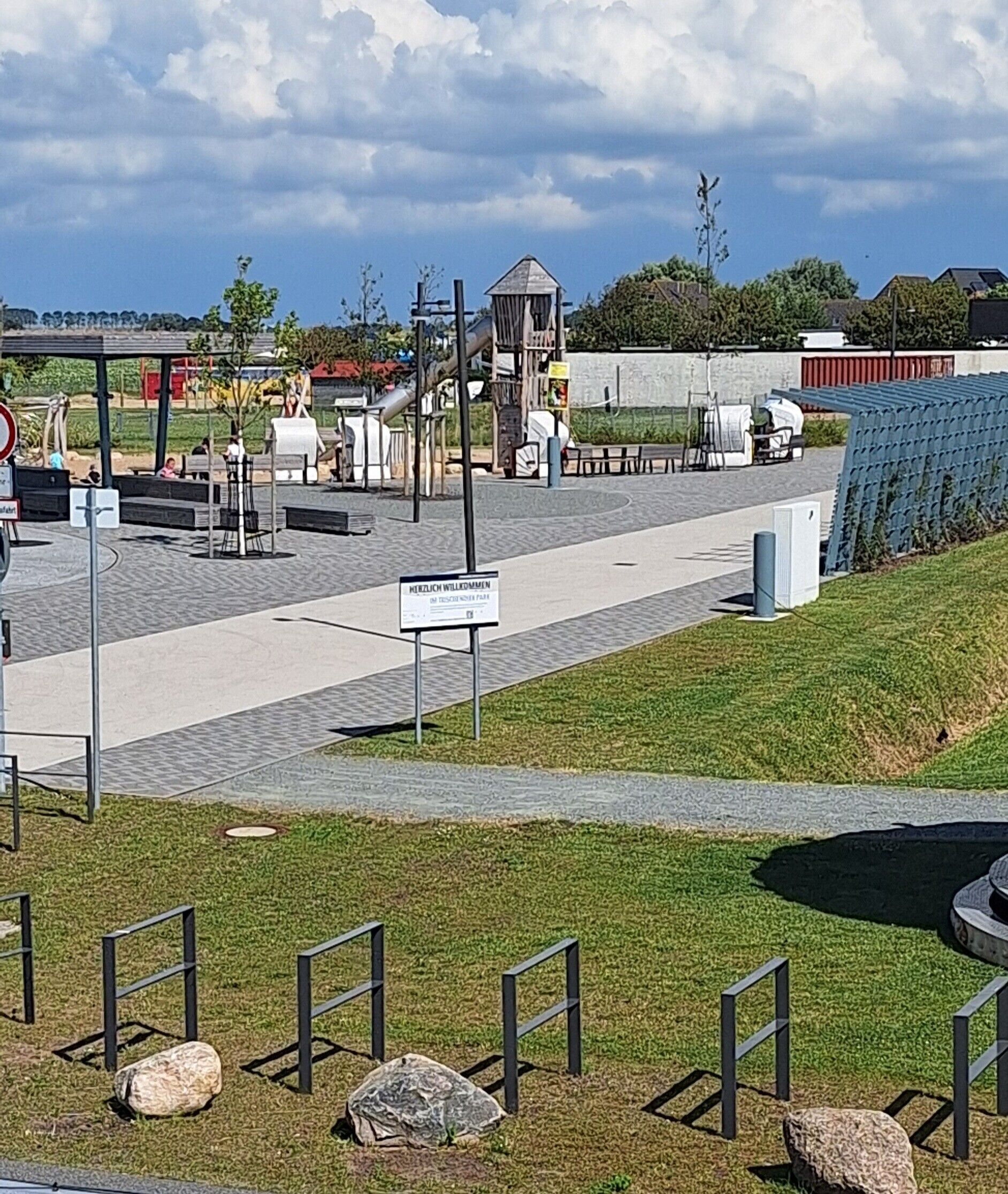 A paved walkway with benches, a playground area, and a sign indicating a memorial.