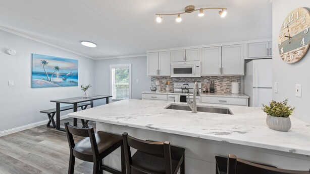 A modern kitchen with white cabinets, a marble island, and a dining area with a table and chairs. - Completely remodeled 3BR/2BA,PET friendly,5min from Hurlburt Field,fully fenced (Mary Esther)