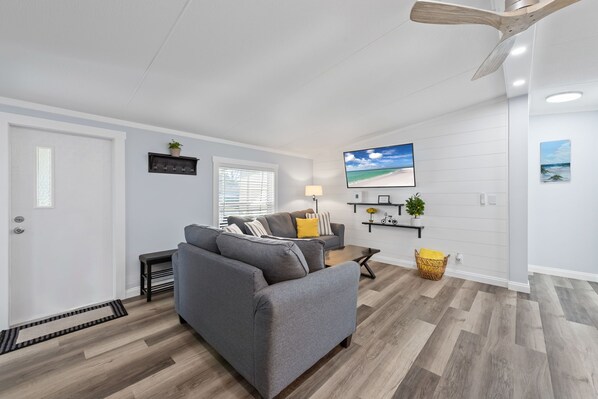 A modern living room with a grey sectional sofa, a small side table, a floor lamp, and a ceiling fan. - Completely remodeled 3BR/2BA,PET friendly,5min from Hurlburt Field,fully fenced (Mary Esther)