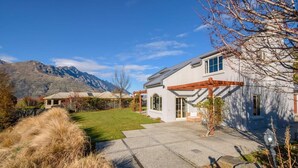A modern house with a large patio, a garage, and a mountain backdrop.