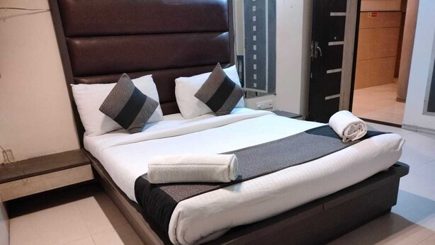 A neatly made bed with a dark headboard, white bedding, and a grey blanket. - HOTEL AL ZAM ZAM (Nagpur)
