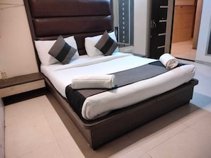 Una cama bien hecha con un cabecero oscuro, ropa de cama blanca y una manta gris.