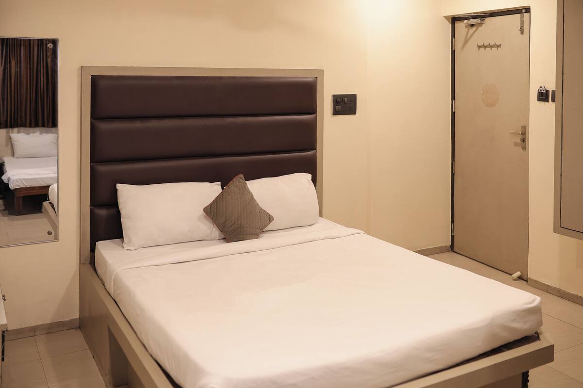 A neatly made bed with a headboard, a bedside table with a lamp, and a door with a lock.