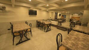 A spacious dining area with multiple tables and chairs, a flat-screen TV mounted on the wall, and a modern ceiling design. - HOTEL AL ZAM ZAM (Nagpur)