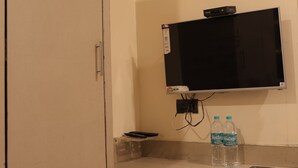A hotel room with a closed door, a mounted flat-screen TV, a small table with two water bottles, and an air conditioning unit on the wall. - HOTEL AL ZAM ZAM (Nagpur)