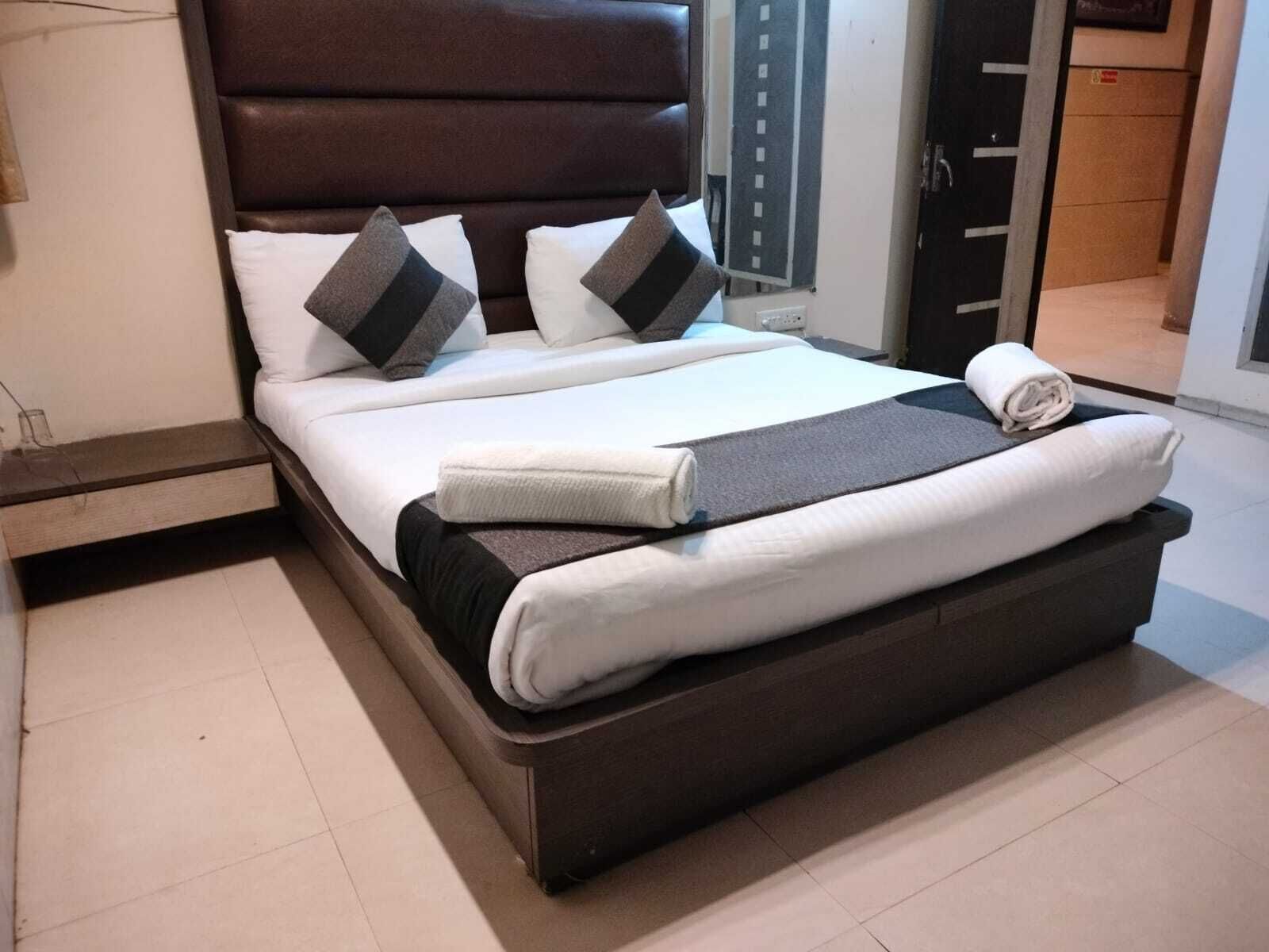 A neatly made bed with a dark headboard, white bedding, and a folded towel on the footboard.