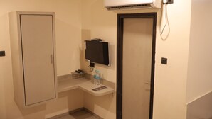 A small room with a white cabinet, a flat-screen TV mounted on the wall, a water dispenser, and a door with a phone receiver. - HOTEL AL ZAM ZAM (Nagpur)
