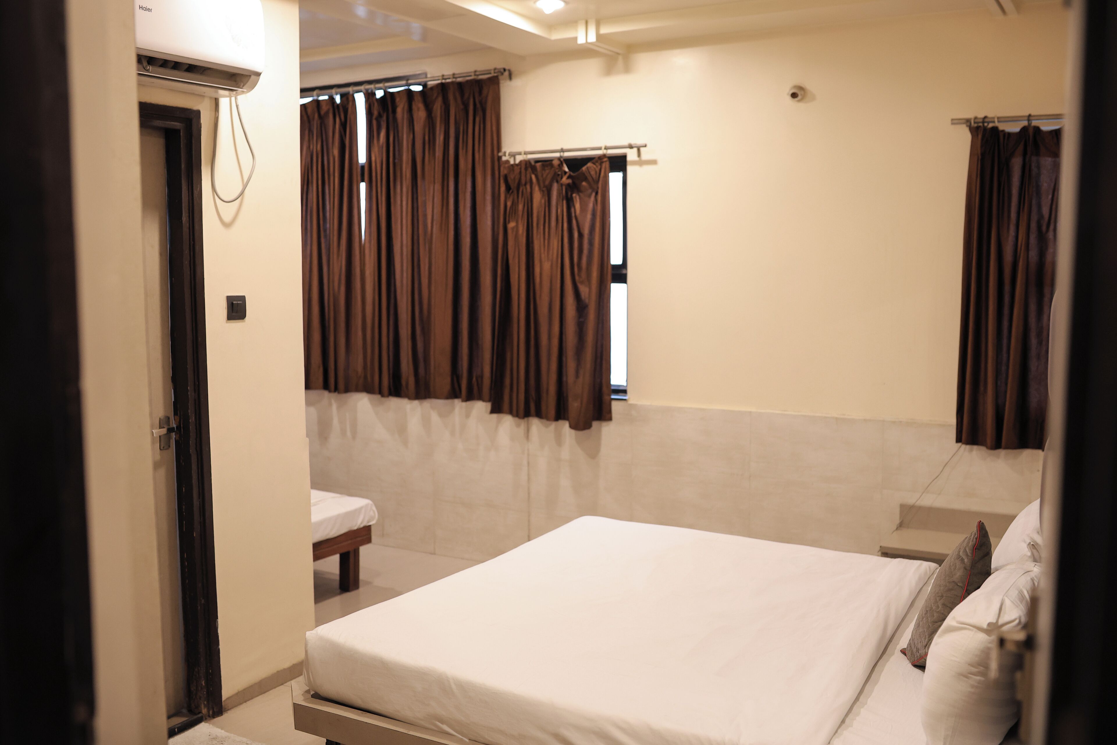 Quarto de hotel com cama, mesa de cabeceira, janela com cortinas e ar condicionado fixado na parede.