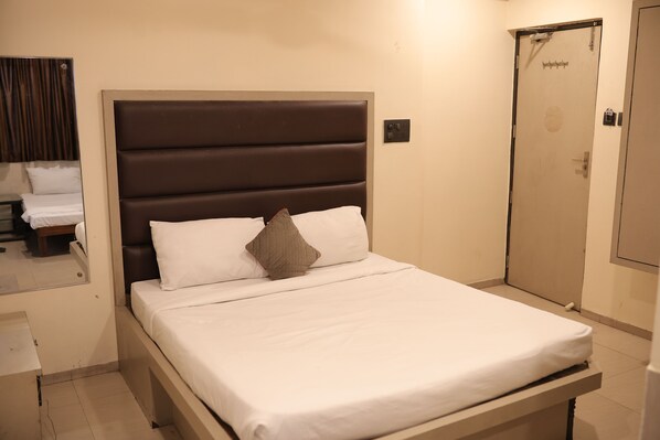 Una cama bien hecha con sábanas blancas y una almohada marrón, una mesita de noche y una puerta con pomo.