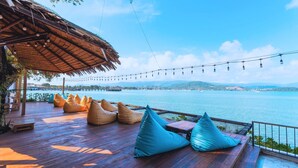 A wooden deck with seating, a thatched roof, and string lights. - Sea Sun Bed & Beyond (Koh Samui)